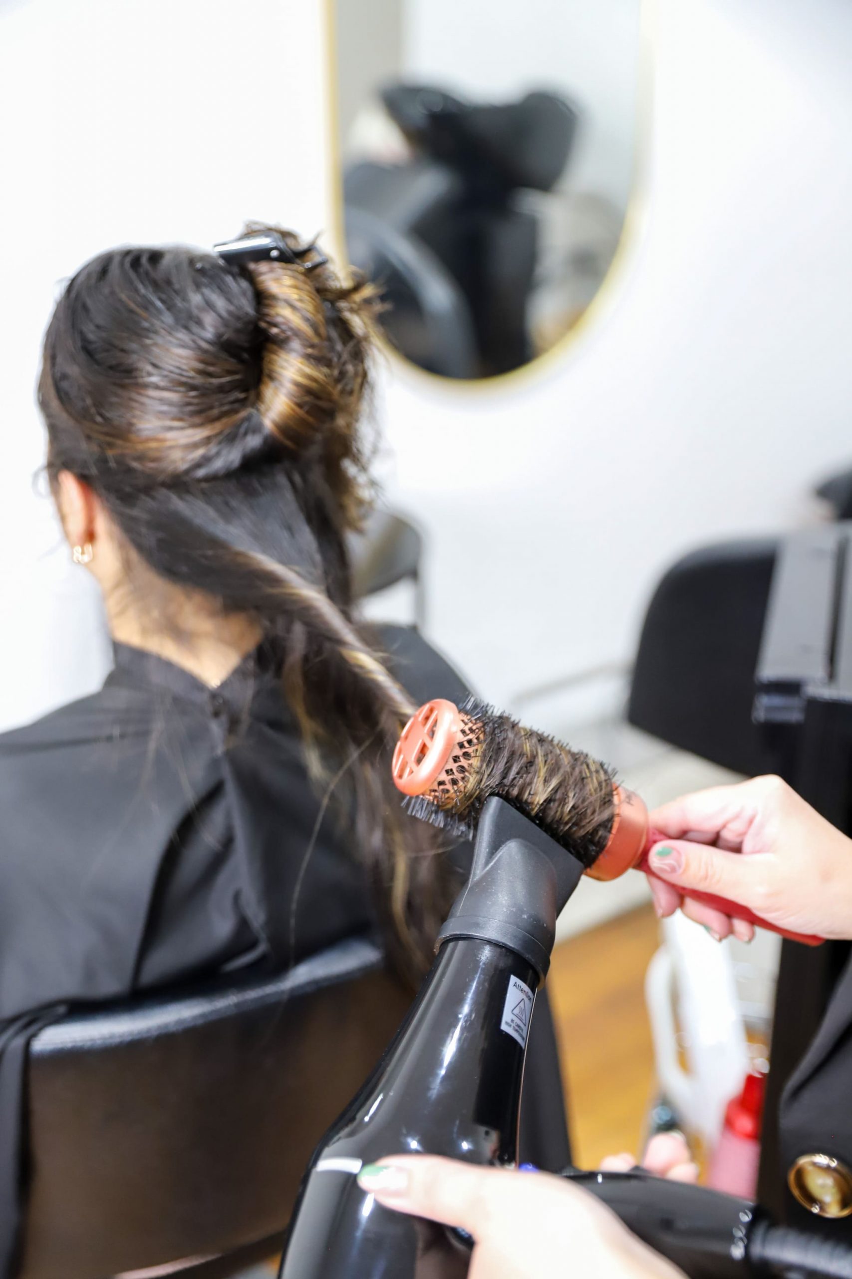Una persona recibiendo un peinado con secador y cepillo redondo en una peluquería.